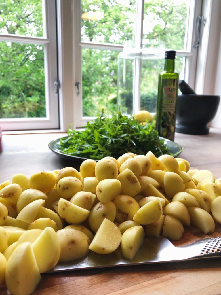 forberedelse af kartofler til kartoffelsalat med rucola Kartoflerne er skåret i tern og ligger på et skærebræt. I baggrunden ses rucola og en flaske olivenolie