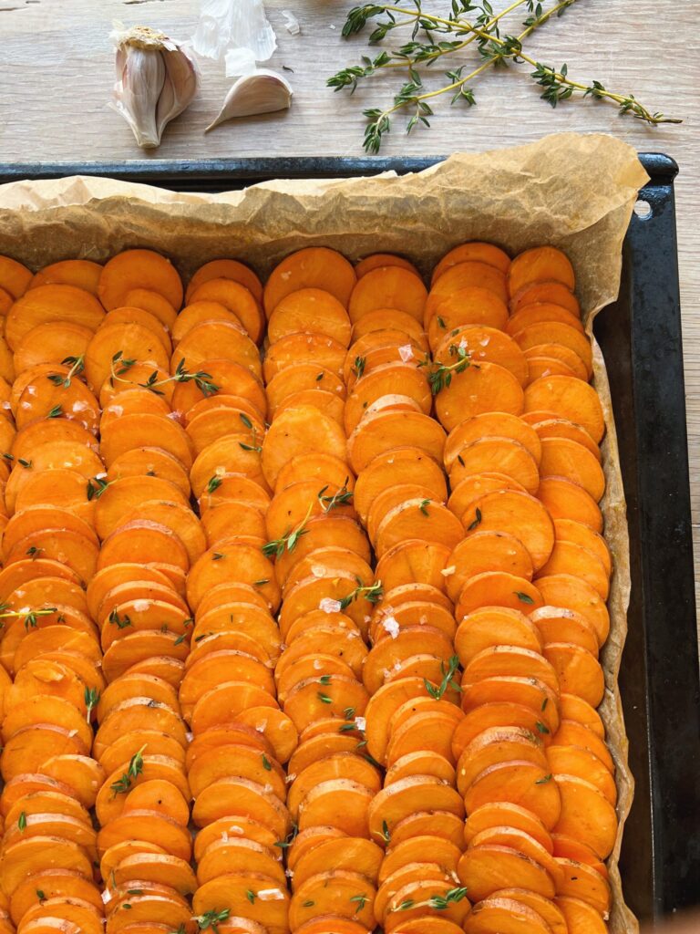 de søde kartofler er lagt i rækker på en bradepande inden de skal bages til opskriften på søde bagte kartofler med smuldret feta