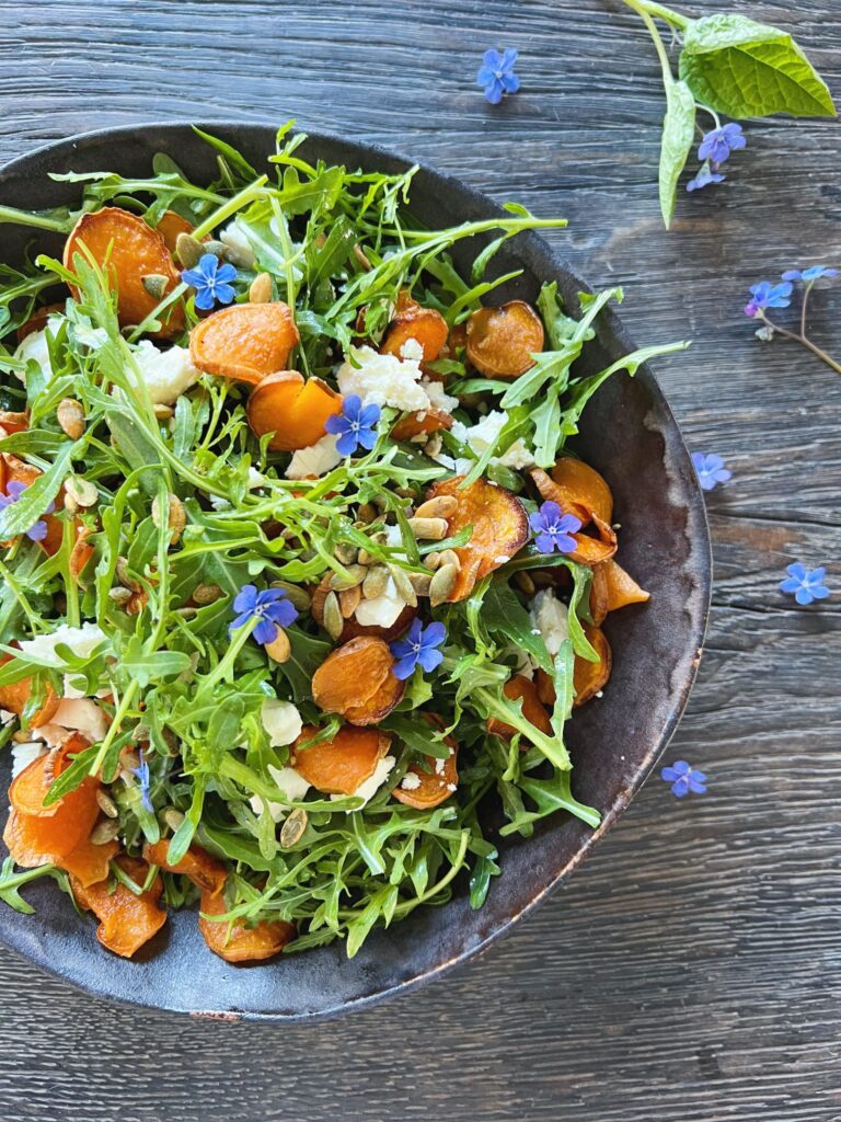 Bagte sode kartofler vist hvor de er brugt i en salat med rucola og saltristede græskarkerner
