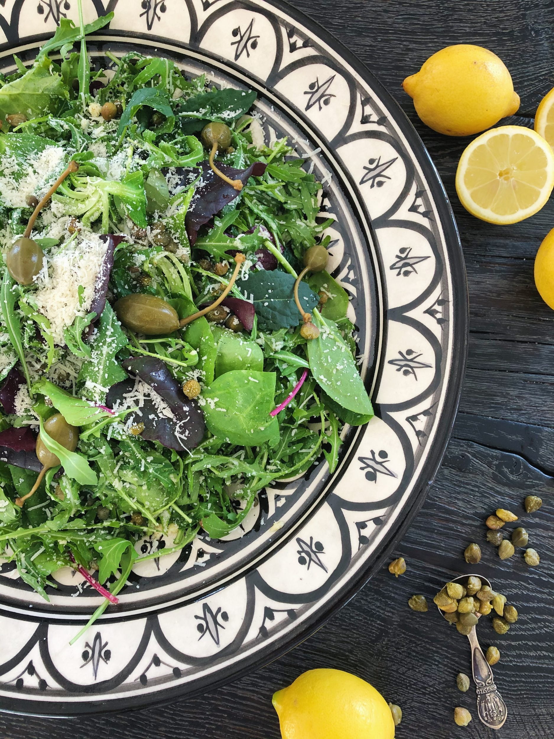 Rucolasalat med kapers, parmesanost og citrondressing ses serveret i et marrokansk fad med sort og hvidt mønster