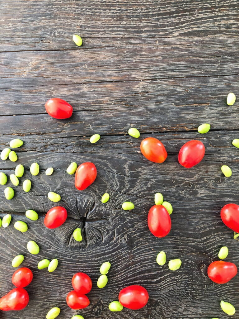 Ingredienser til tomatsalat med edamamebønner. På et sort rustikt bord ser edamamebønner og cherrytomater spredt placeret.