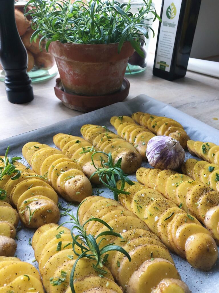 Kartoffelskiver lagt i rækker på bageplade med krydderurter og hvidløg