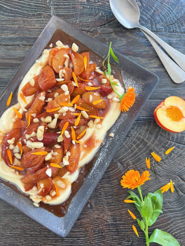Ovnbagte ferskner serveret med cremet mascarpone og toppet med mandler og kronblade fra morgenfrue – en nem og smuk sommerdessert