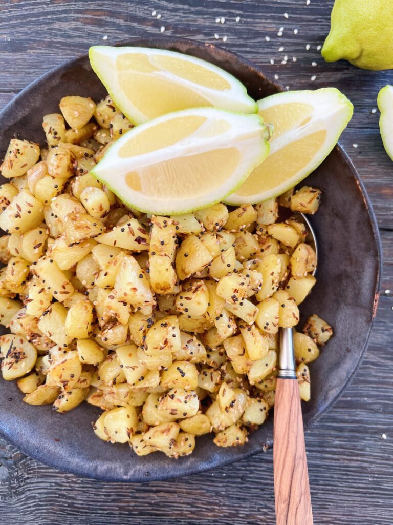 brasede kartofler i rustik keramikskål med citronbåde og en ske med skaft i oliventræ