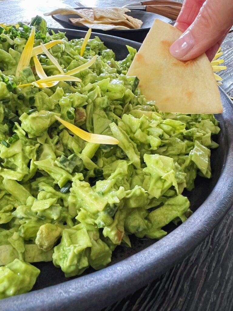 grøn salat med grøn dressing i sort rundt keramikfad på sort træbord hvor man ser en hånd med en tortilla der skal til at tage en smagsprøve