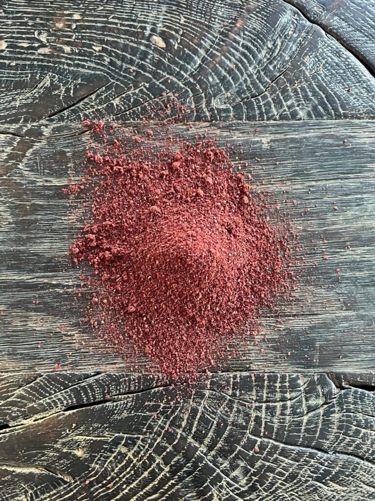 En bunke af det røde stødte krydderi sumac på et sort, rustikt træbord, klar til at blive brugt i en salat med yoghurtdressing.