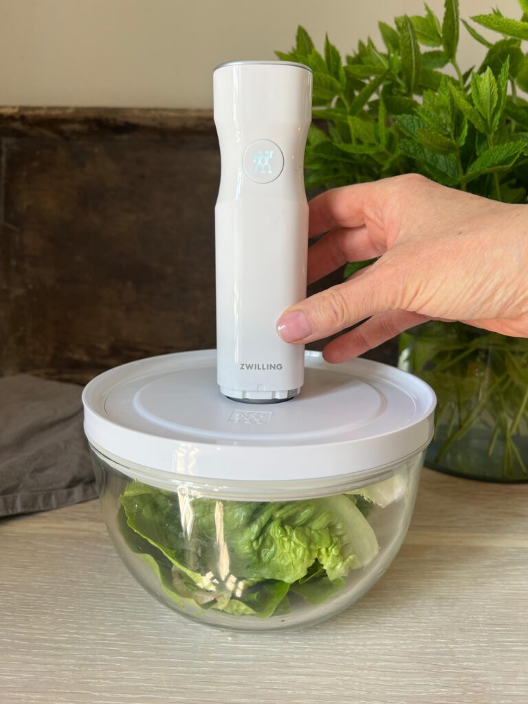 salat til aspargessalat er ved at blive vakuumpakket i en glasskål. En hånd støtter vakuumpumpen som er hvid. Det er fra fresh and save serien fra Zwilling