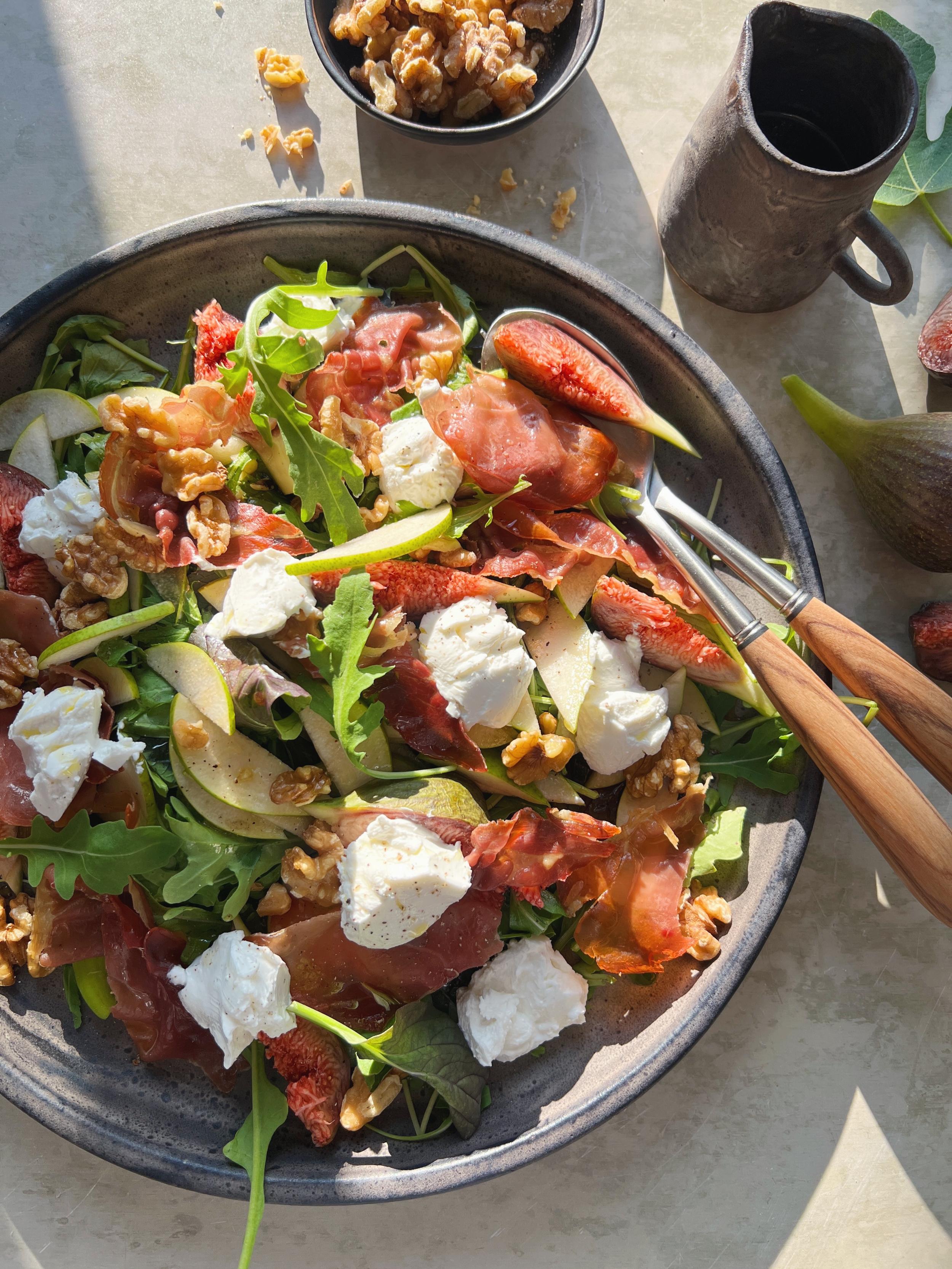 Salat med figner, pærer, spæd salat, rucola, gedeost, parmaskinke og valnødder serveret i fad.